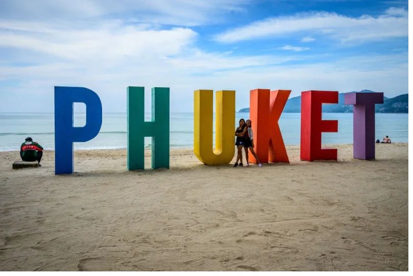Những người phụ nữ chụp ảnh trước một bảng hiệu tại Bãi biển Patong trên đảo Phuket của Thái Lan vào ngày 28 tháng 10 năm 2021, khi đất nước chuẩn bị chào đón những du khách được tiêm chủng đầy đủ vắc xin chống lại coronavirus Covid-19 mà không cần kiểm dịch từ ngày 1 tháng 11.