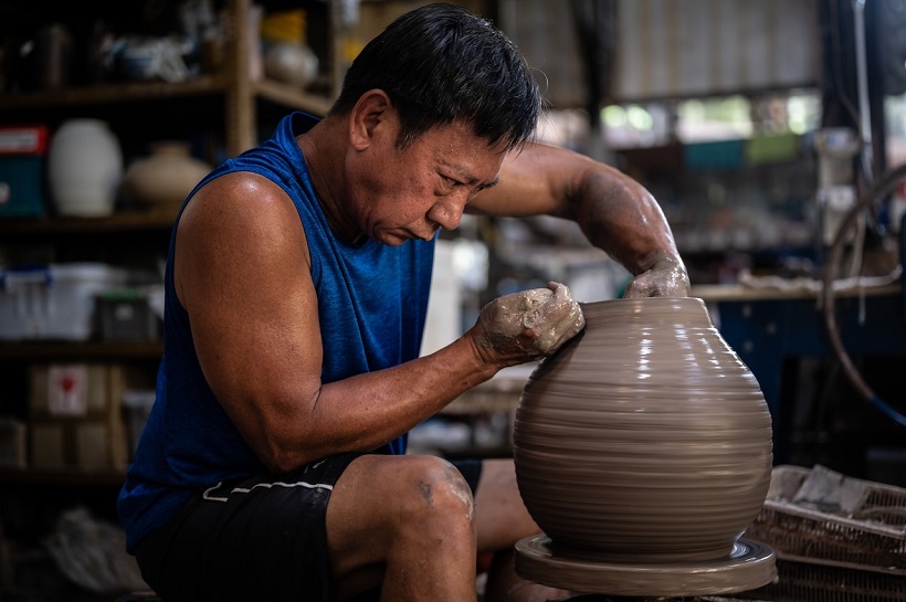 Một nghệ nhân đang tập trung cao độ khi kéo đất sét trên bánh xe của thợ gốm tại Thow Kwang Pottery Jungle.