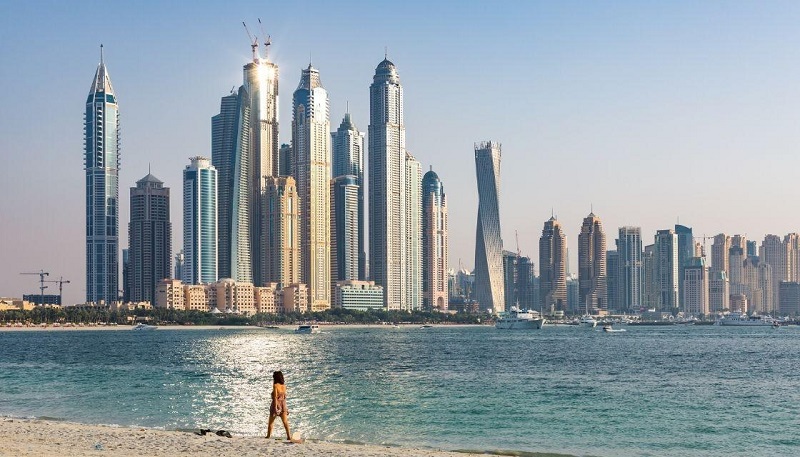 Người phụ nữ đi dạo trên bãi biển phía trước đường chân trời của Dubai.