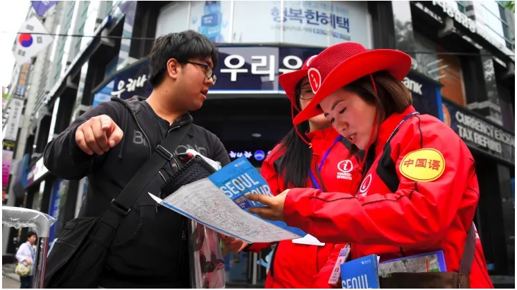 Những người trợ giúp thông tin Tour du lịch Hàn Quốc hướng dẫn khách du lịch tại khu mua sắm Myeongdong nổi tiếng của Seoul.